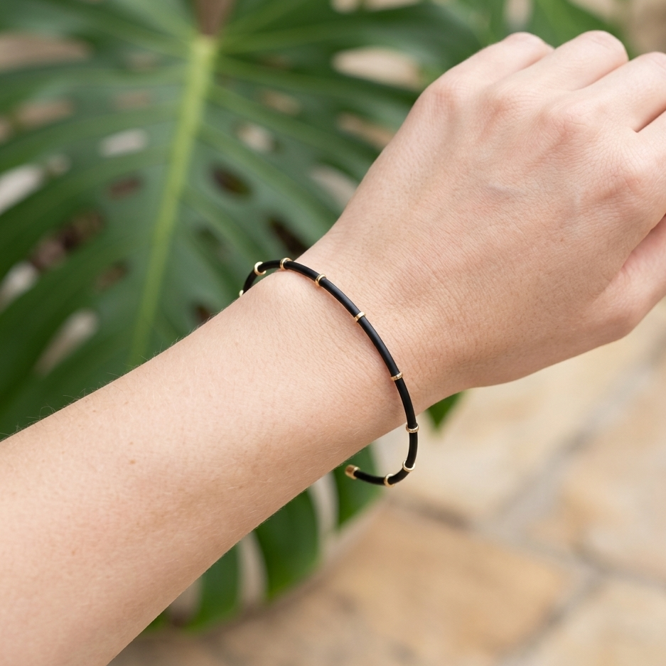 Jonc Mara bracelet fin émail noir doré porté au poignet femme extérieur végétation tropicale KD Softy Bijoux
